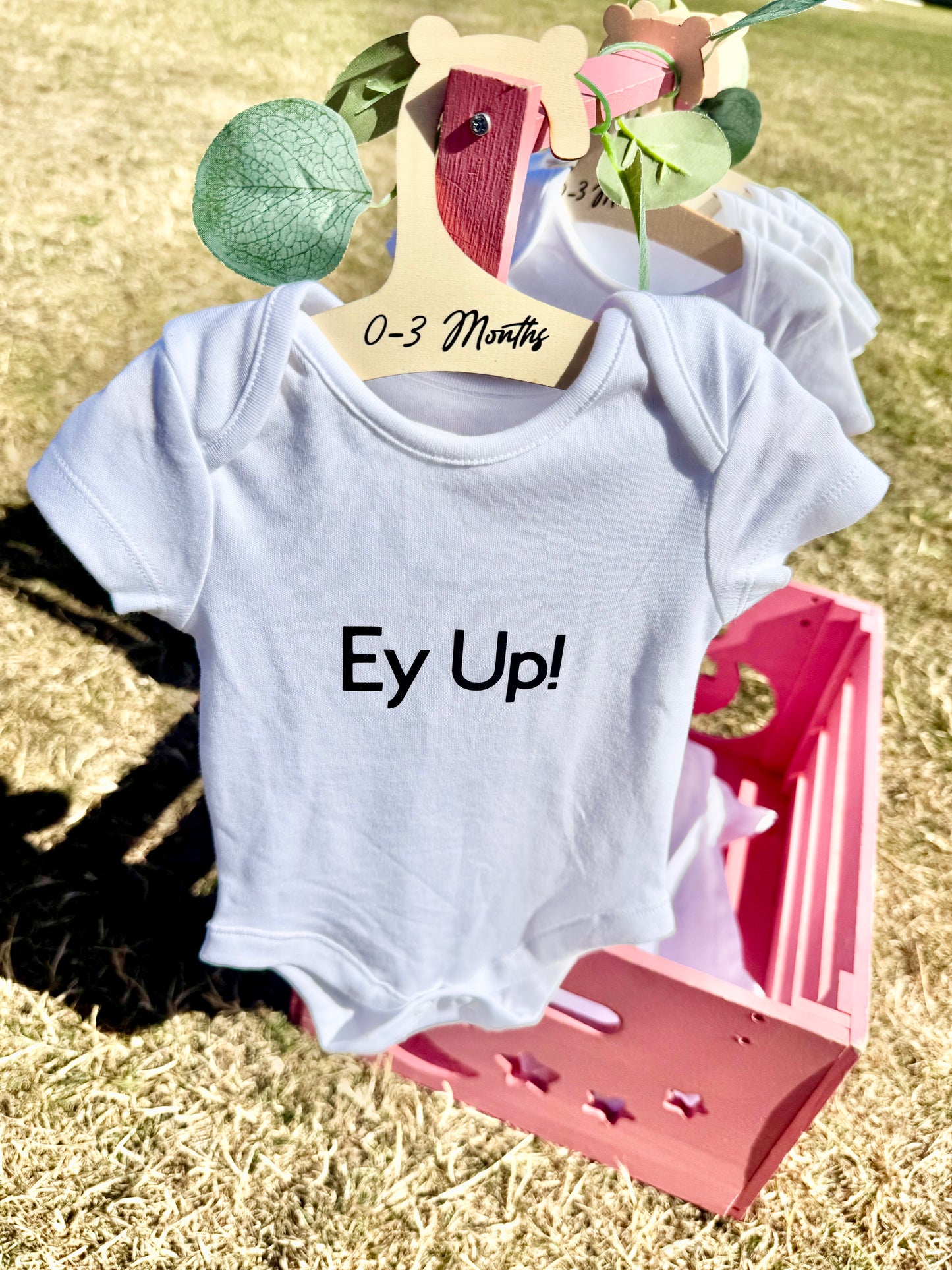 White baby bodysuit with bold black text that reads “Ey Up, Baby!” displayed flat on a neutral background, ideal for newborns and Yorkshire-themed baby gifts.