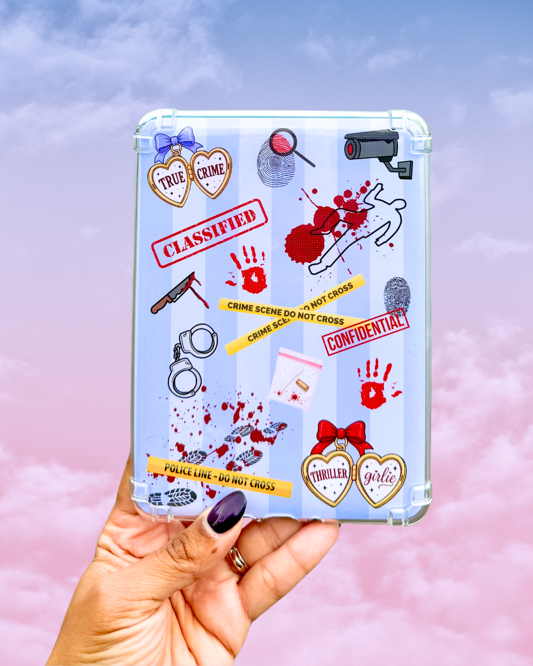 A hand with dark purple nail polish holds a tablet case decorated with a true crime theme, featuring stickers like 'True Crime' hearts, 'Classified' and 'Confidential' stamps, blood splatters, and handcuffs, set against a pink and blue cloudy sky background.