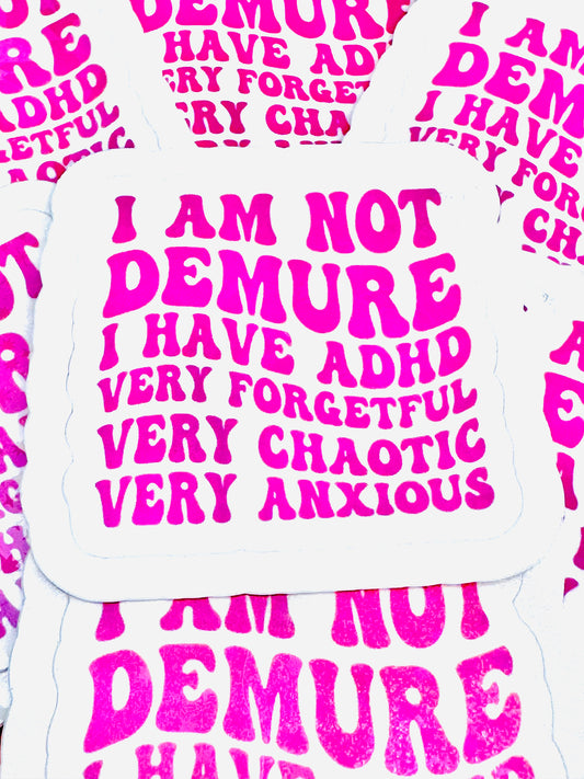 White vinyl sticker with the phrase ‘I am not demure I have ADHD – very forgetful, very chaotic, very anxious’ in pink font, photographed on a flat surface.
