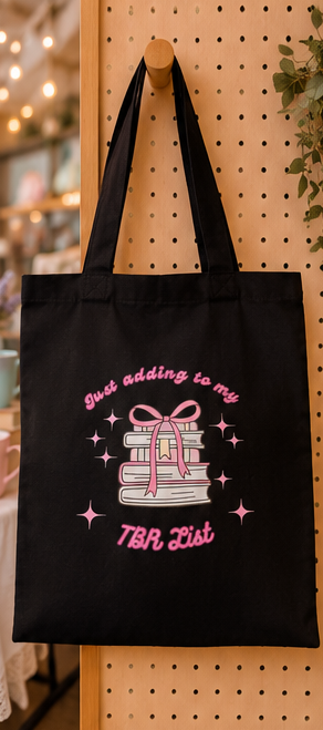 Black canvas tote bag with pink “Adding To My TBR List” design featuring stacked books, bows and sparkly bookish artwork.