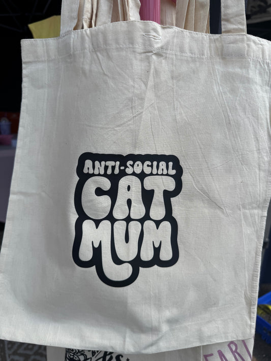 A white tote bag with the text 'ANTI-SOCIAL CAT MUM' printed in black.