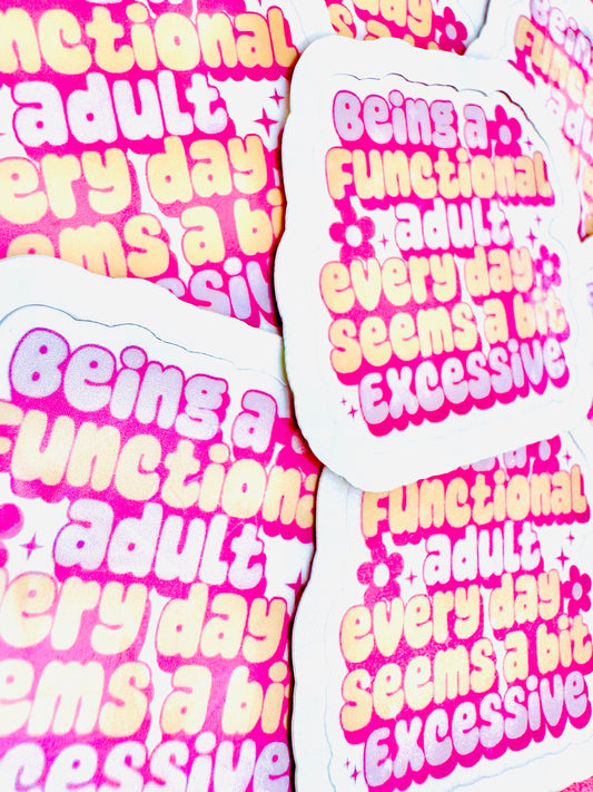 White vinyl sticker with the phrase ‘Being a functional adult every day seems a bit excessive’ in pink and peach font, photographed on a flat surface.