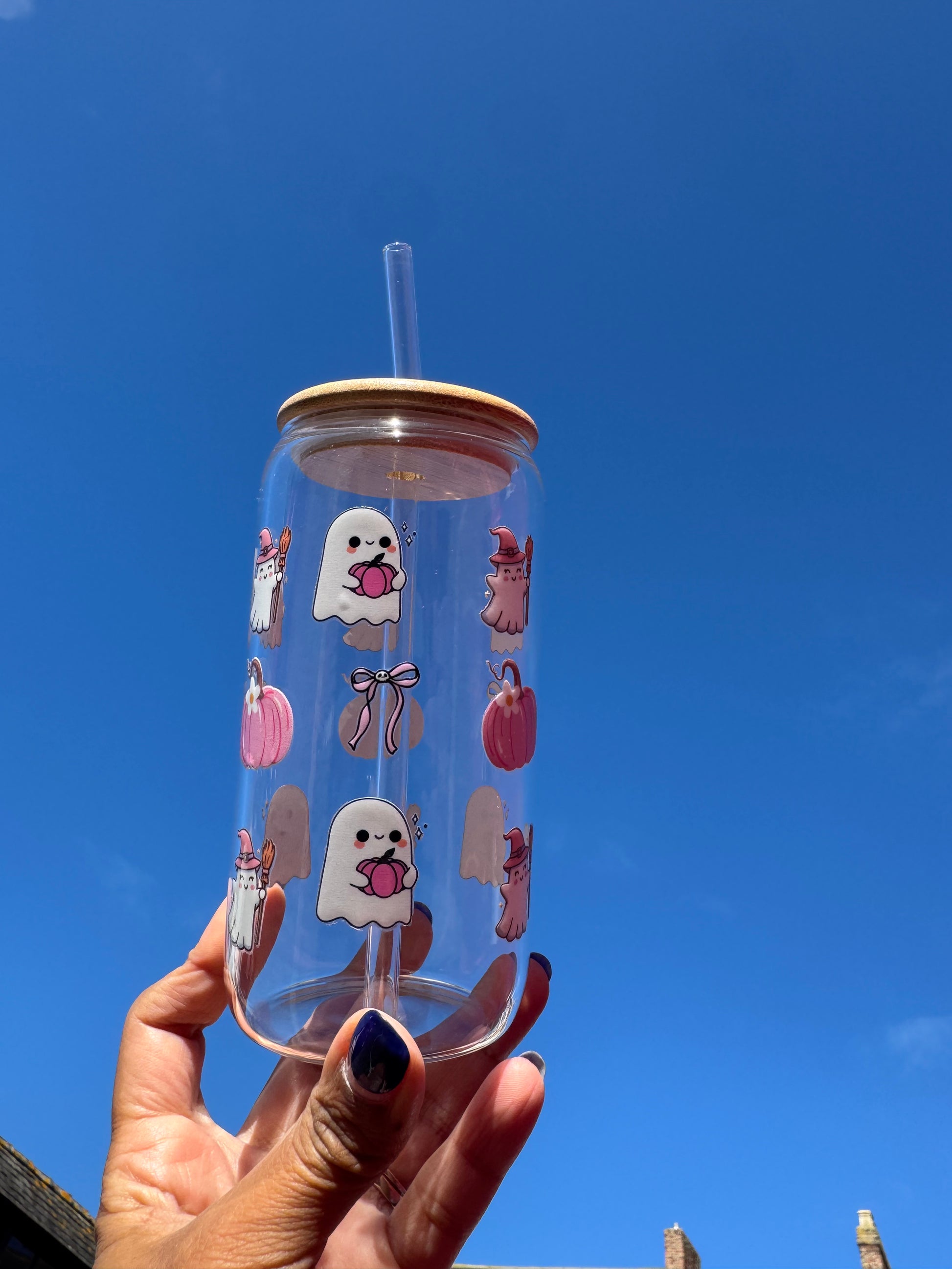 "A clear glass can cup with a spooky-cute Halloween design: a boo ghost holding a pink pumpkin, pink bows with skulls, pink pumpkins, and a ghost witch."