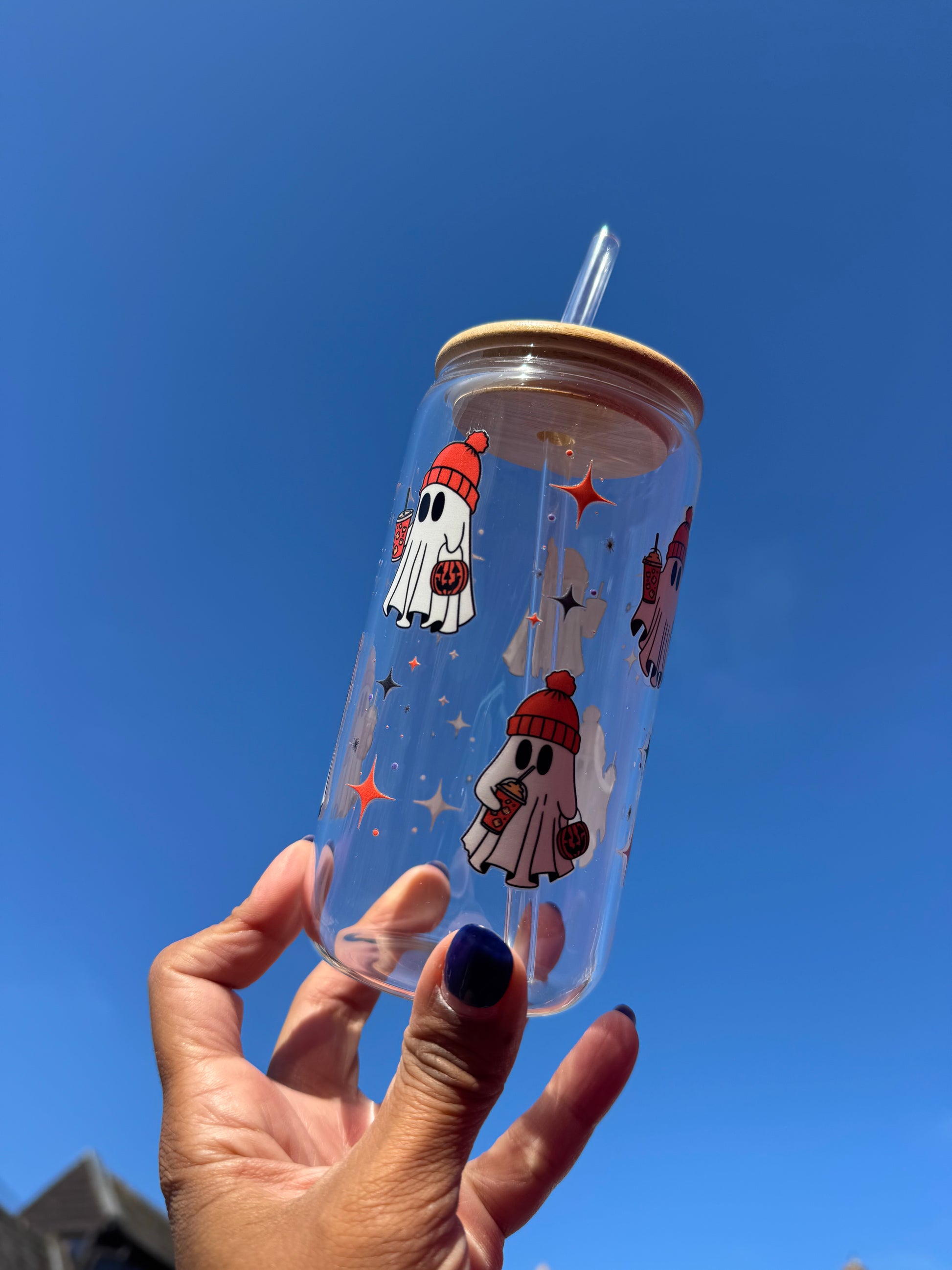 "A clear glass can cup with cute white ghosts holding pumpkin spice lattes and orange pumpkin trick-or-treat bags, perfect for autumn and Halloween drinks."