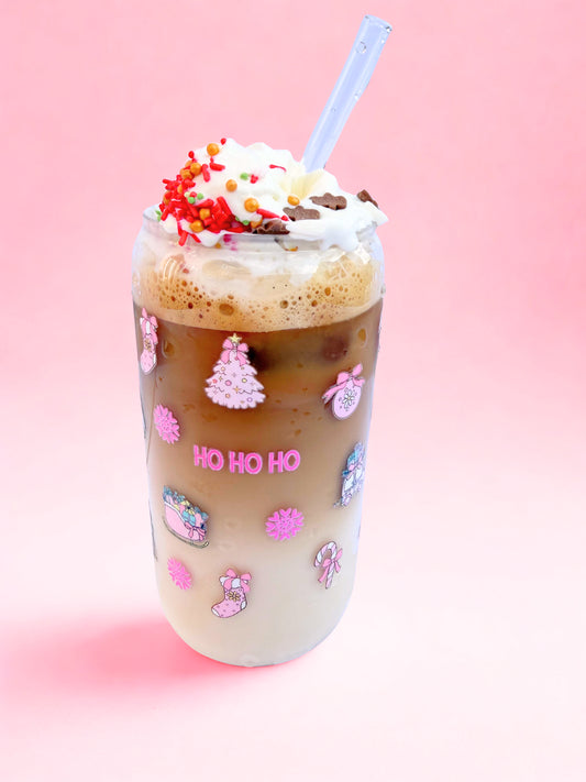 Glass can cup with pink festive image on it, such as ho ho ho, christmas tree and baubles. It is on a pink background