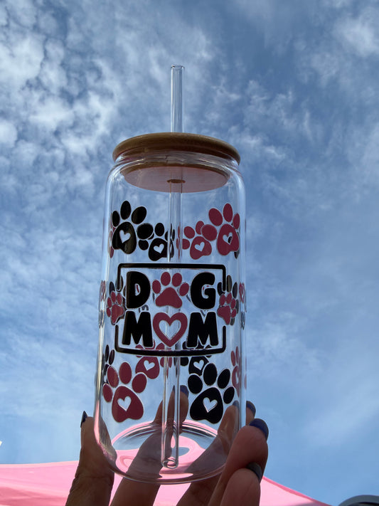 “Clear glass cup with pink and black paw prints and ‘DOG MOM’ text, bamboo lid and glass straw, held up against a blue sky – handmade by JemmaRuth Designs.”