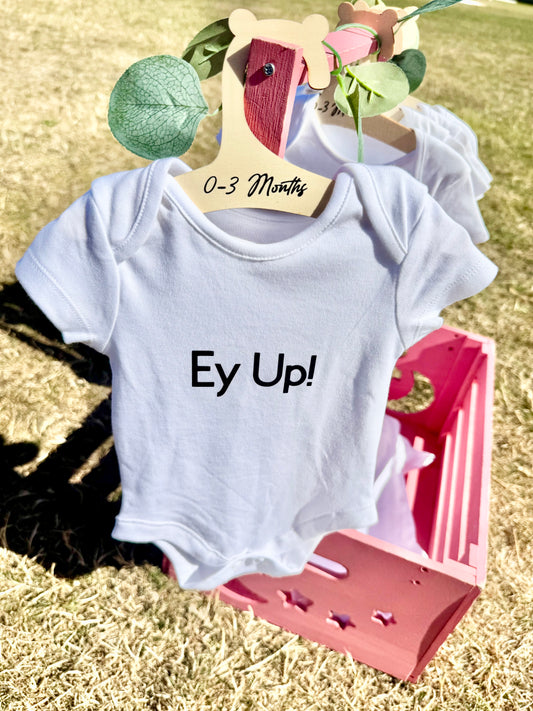 White baby bodysuit with bold black text that reads “Ey Up, Baby!” displayed flat on a neutral background, ideal for newborns and Yorkshire-themed baby gifts.