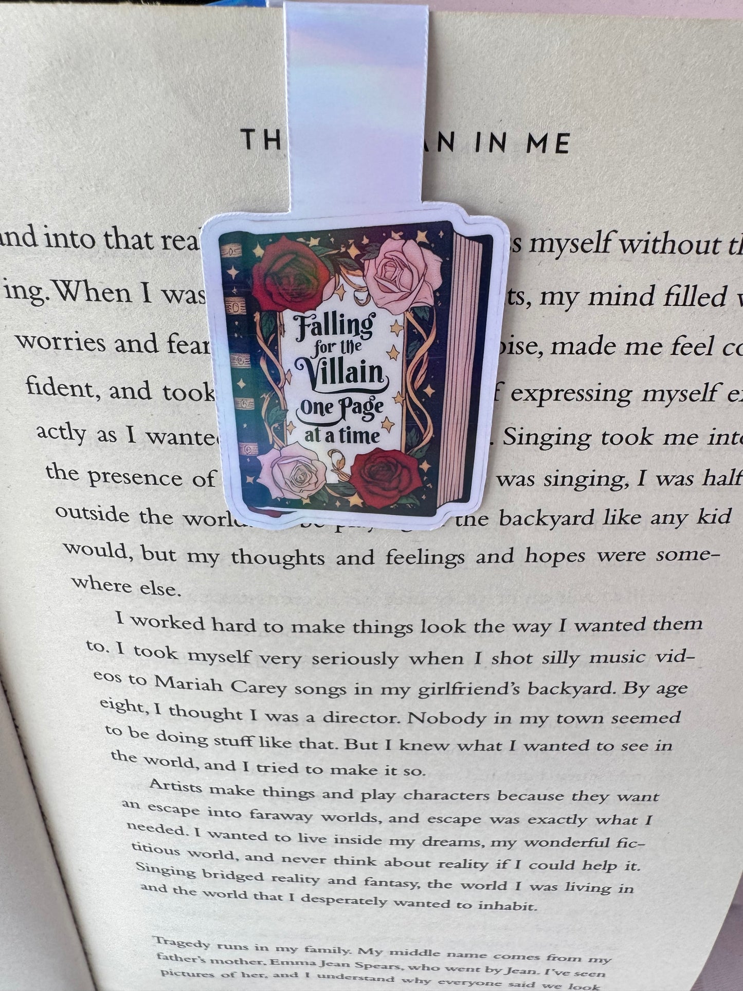 A magnetic bookmark attached to a page on the bookmark is a book with roses on it and the saying falling for the villain one page at a time 