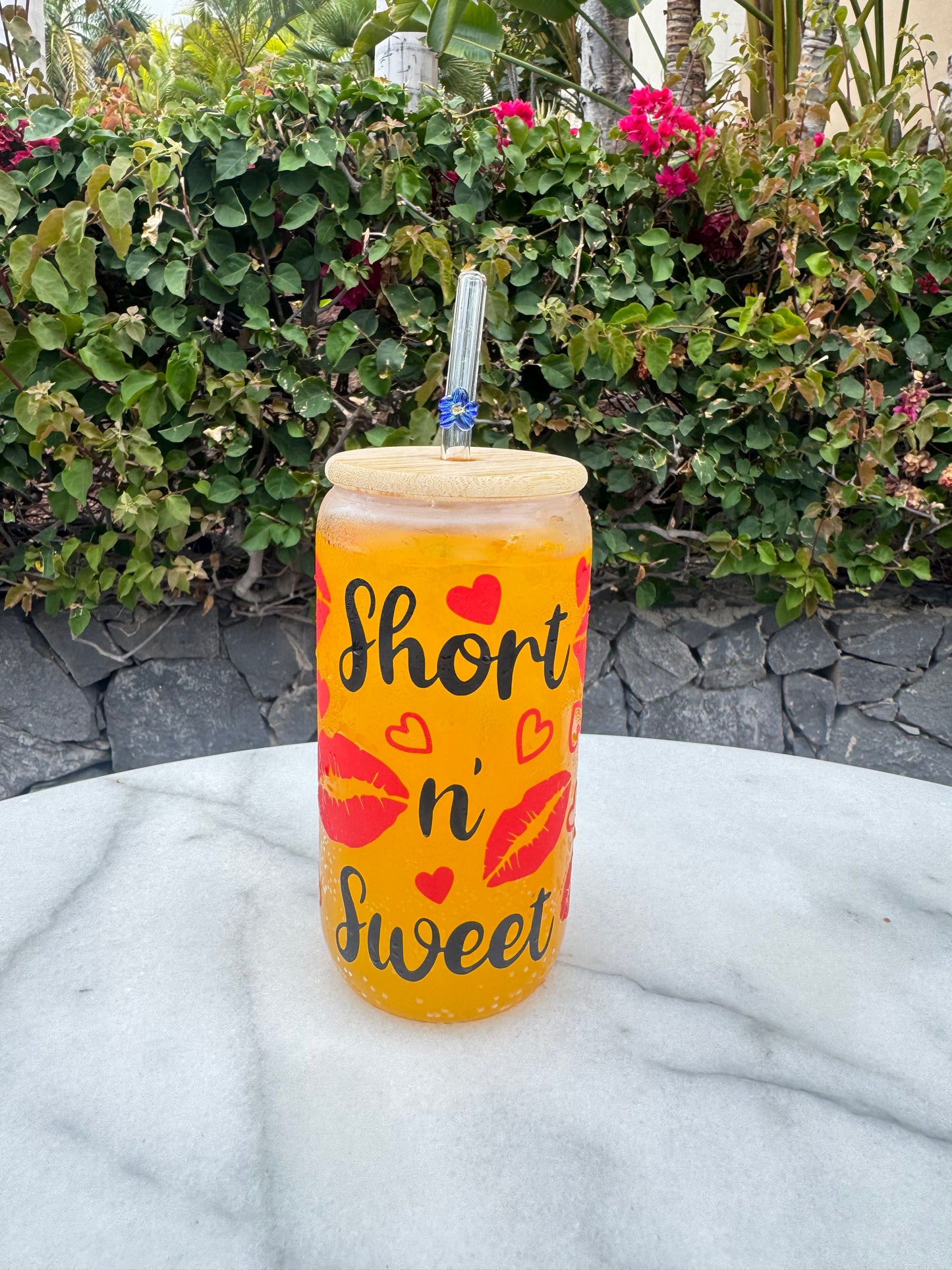 Glass Can Cup with 'short n' sweet' text and red lips design on a stone surface with plants in the background