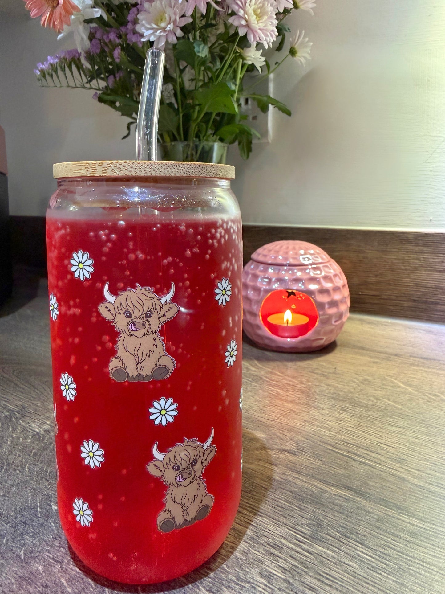 Highland cow glass can cup filled with a fizzy red drink, bamboo lid and glass straw on a kitchen counter.