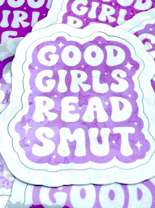 Pink vinyl sticker with the phrase ‘Good Girls Read Smut’ in white font, photographed on a flat surface.