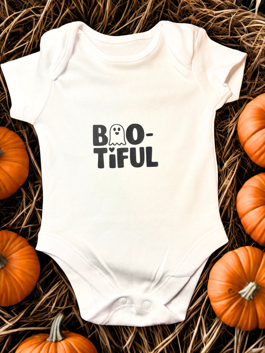 White cotton baby bodysuit with the word “BOO-tiful” in bold black letters, featuring a ghost replacing one of the O’s and heart detail above the I. 