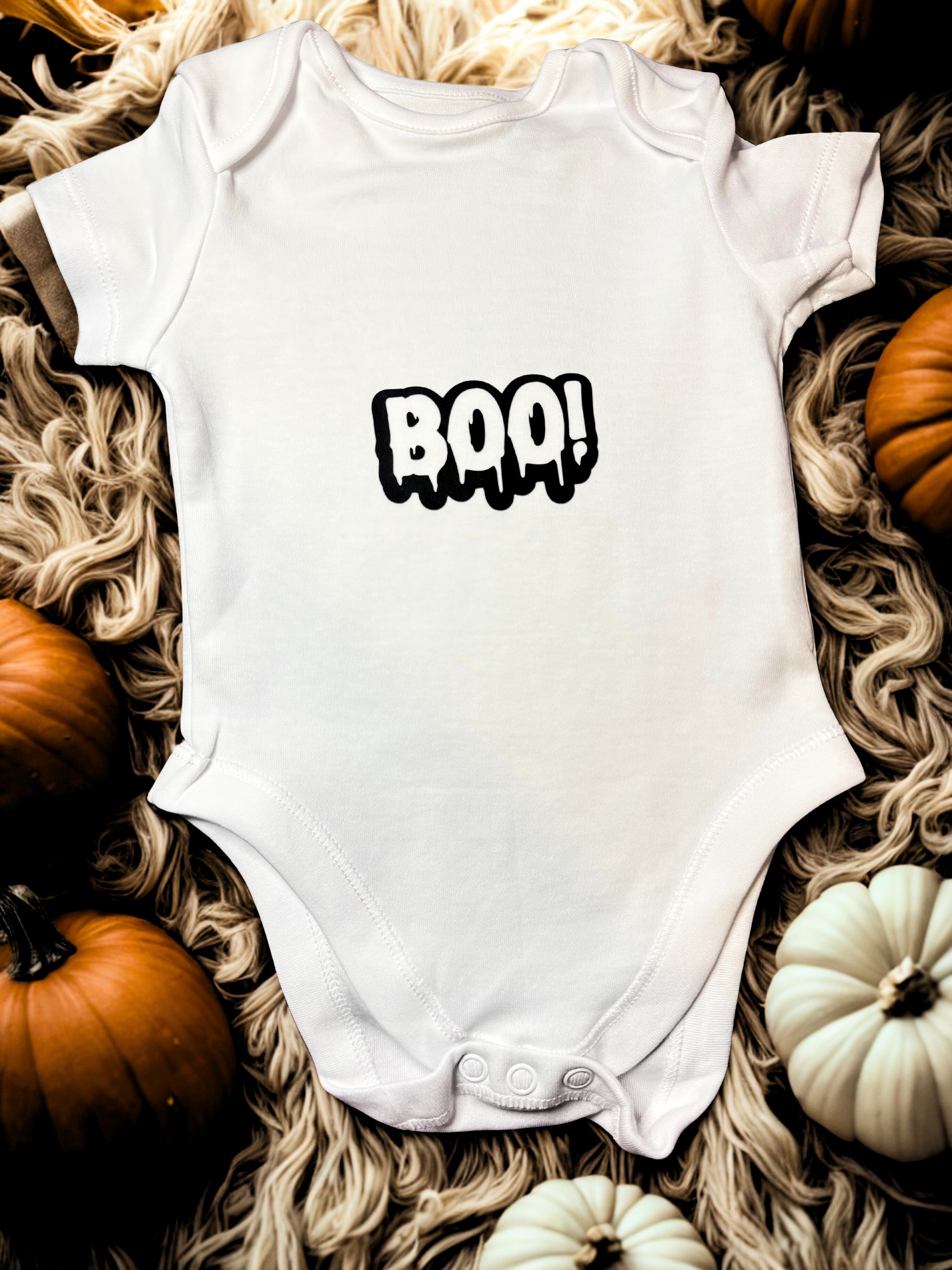 White cotton baby bodysuit with the word “BOO!” in bold black letters.