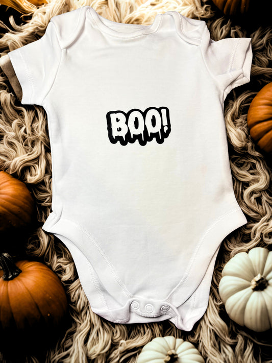 White cotton baby bodysuit with the word “BOO!” in bold black letters.