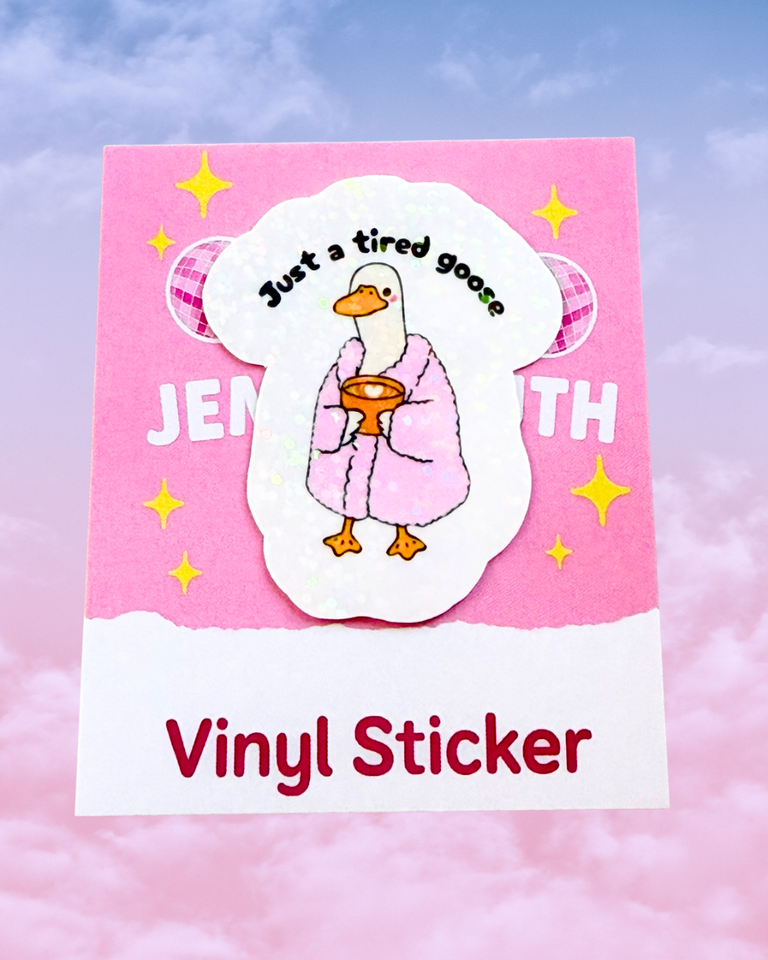 A vinyl sticker featuring a cartoon goose in a pink robe holding a bowl, with the text 'Just a tired goose' above it, presented on a pink backing card that reads 'Vinyl Sticker' against a soft pink sky background.