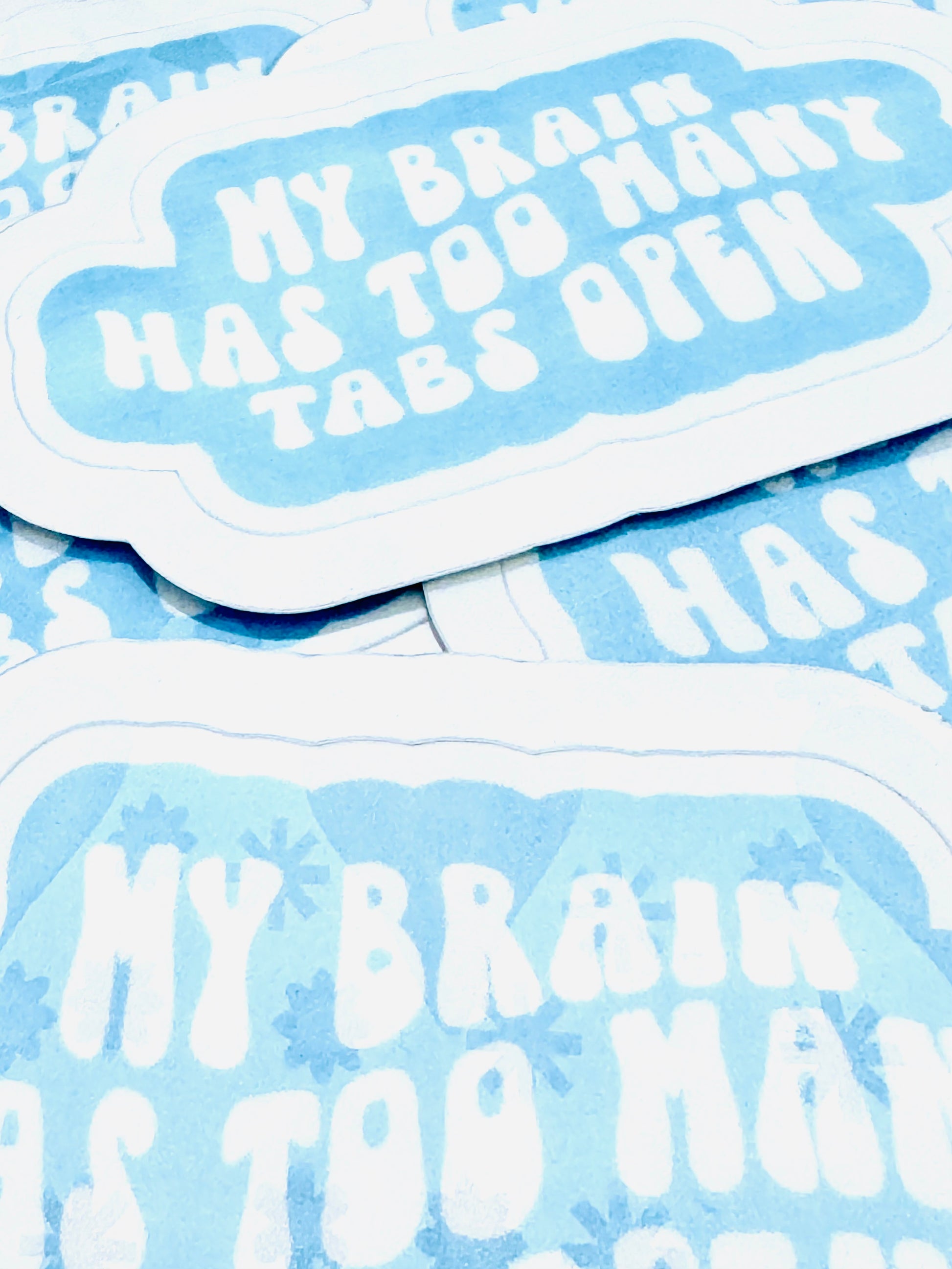 White vinyl sticker with the phrase ‘My Brain Has Too Many Tabs Open’ in baby blue font, photographed on a flat surface.