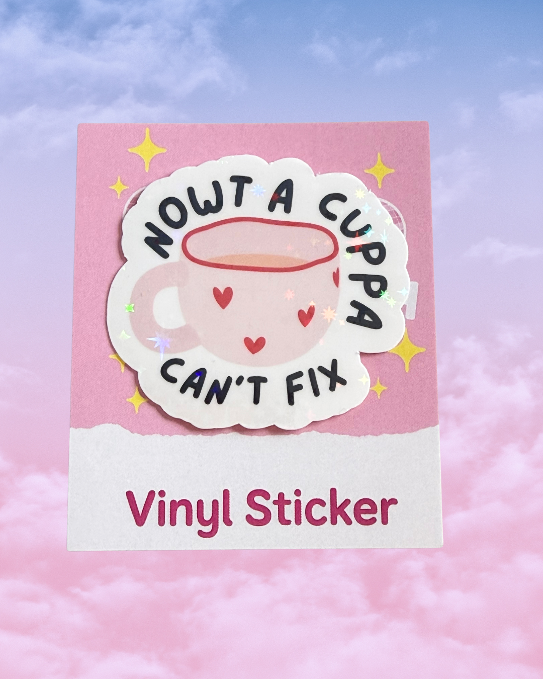 A vinyl sticker featuring a cute pink cup with a halo and the text 'NOWT A CUPPA CAN'T FIX' in black, shown on its pink backing card with 'Vinyl Sticker' printed at the bottom against a pastel pink and blue sky background.