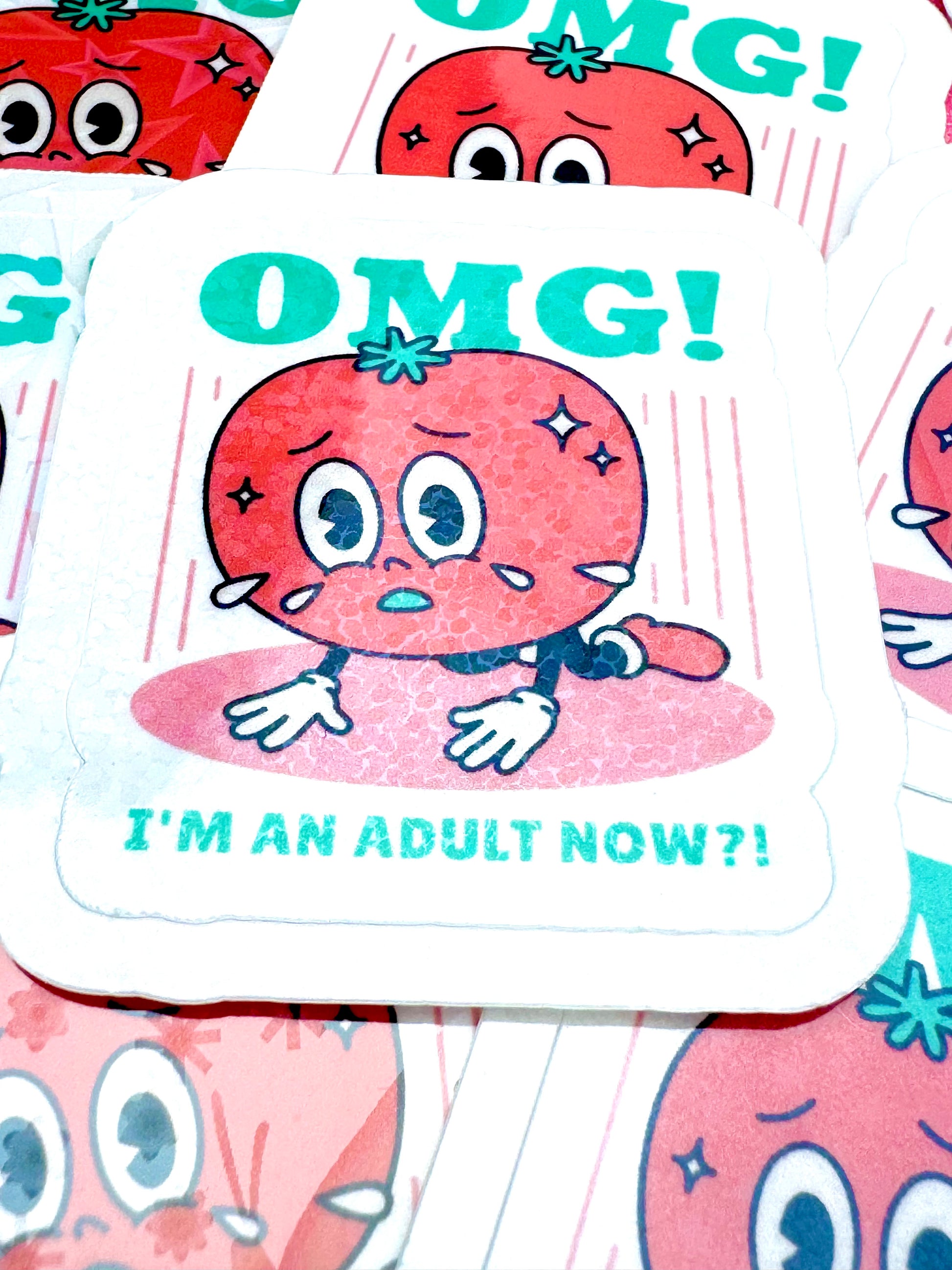 Vinyl sticker showing a cartoon tomato kneeling on the floor with sweat droplets, alongside the phrase ‘OMG! I’m an Adult Now’, photographed on a flat surface