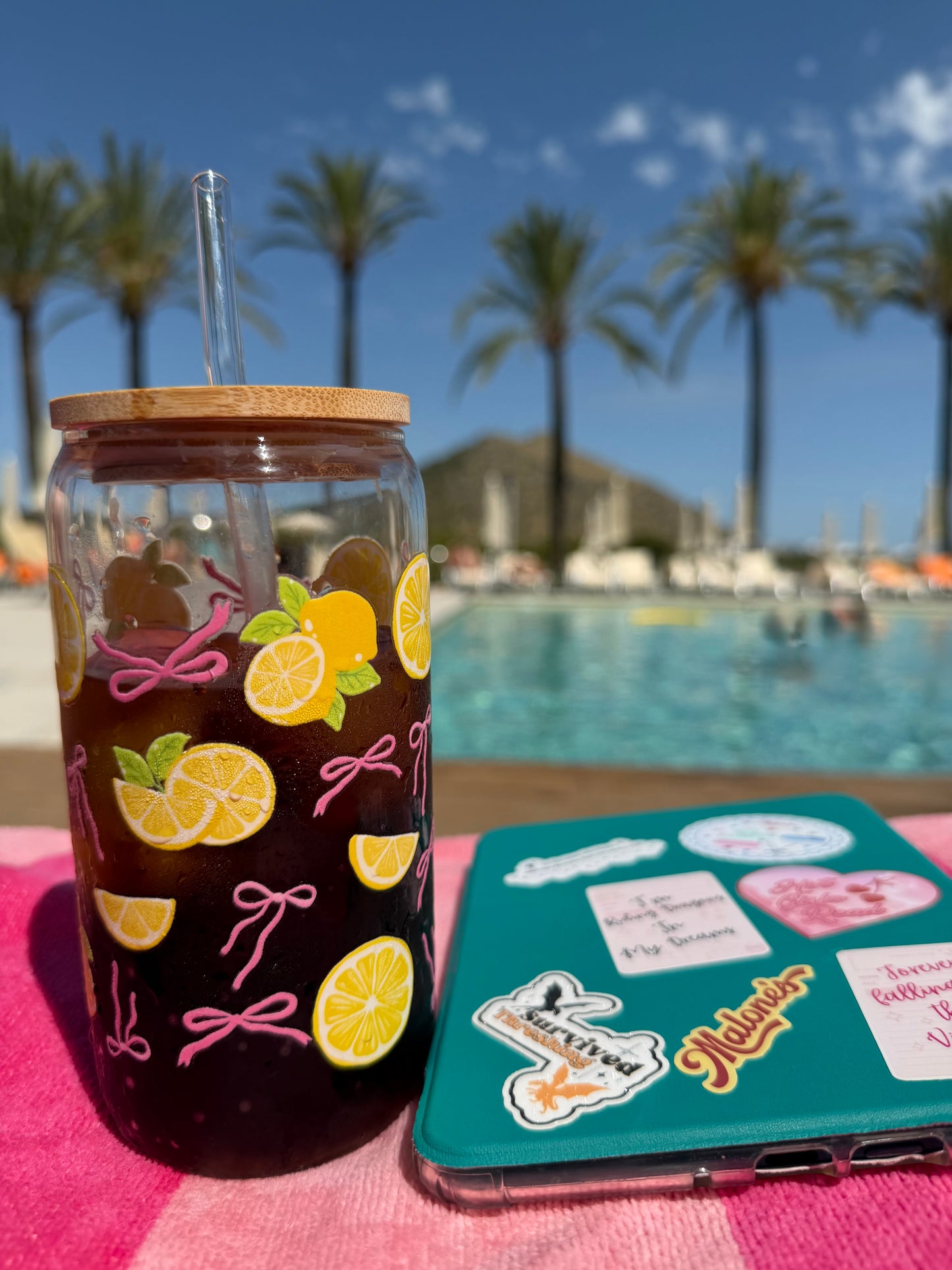 Pink Bows & Lemons Glass Can Cup beside a pool and Kindle, perfect for summer reading days.