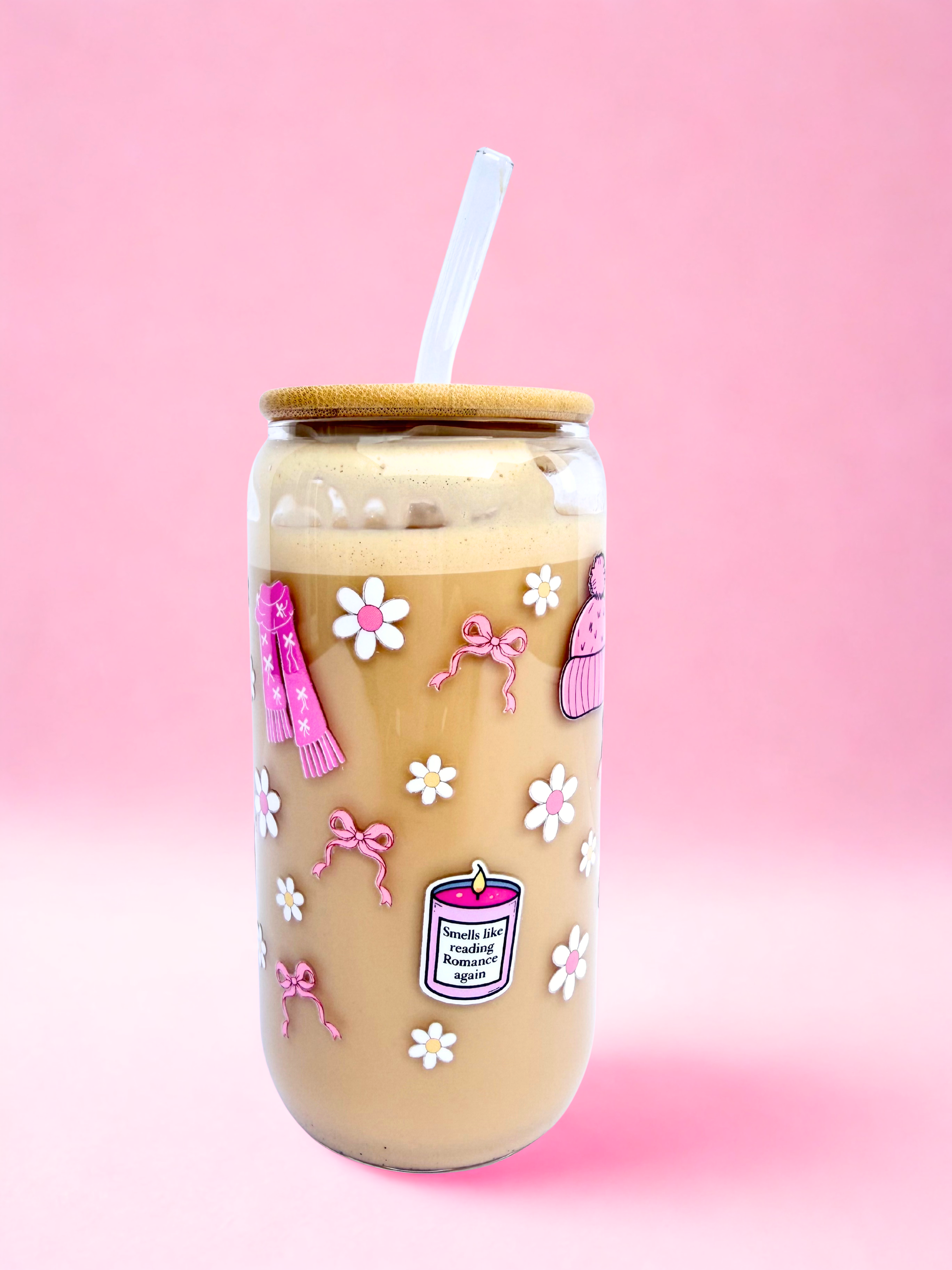 A 16oz glass with a bamboo lid and glass straw, decorated with pink bows, daisies, boots, jumpers, and a candle that says “Smells like reading romance again” on a pink background. Matching bookmark sold separately.