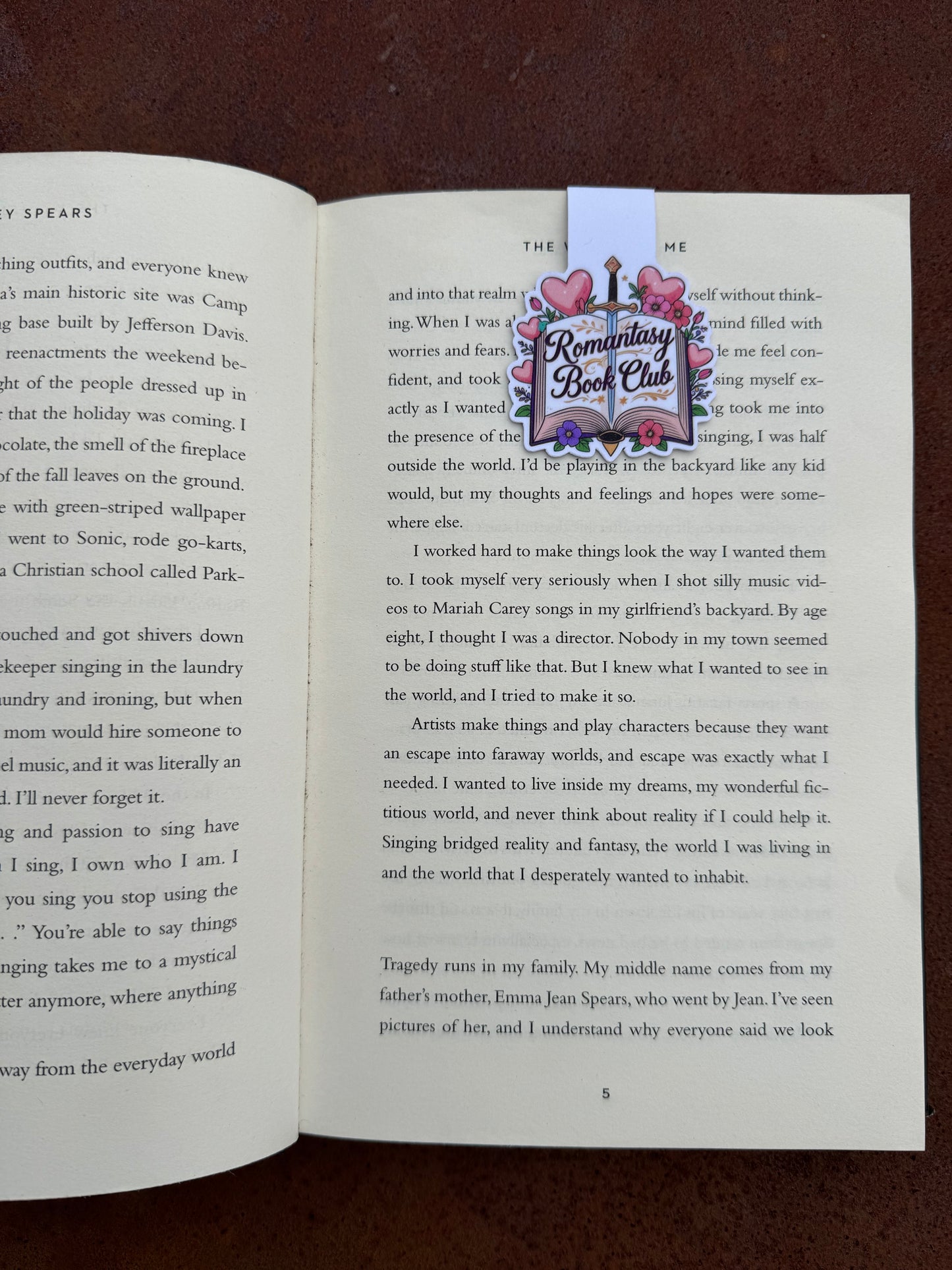 Open book with a magnetic bookmark featuring a colorful design saying Romantasy Book club on a brown surface