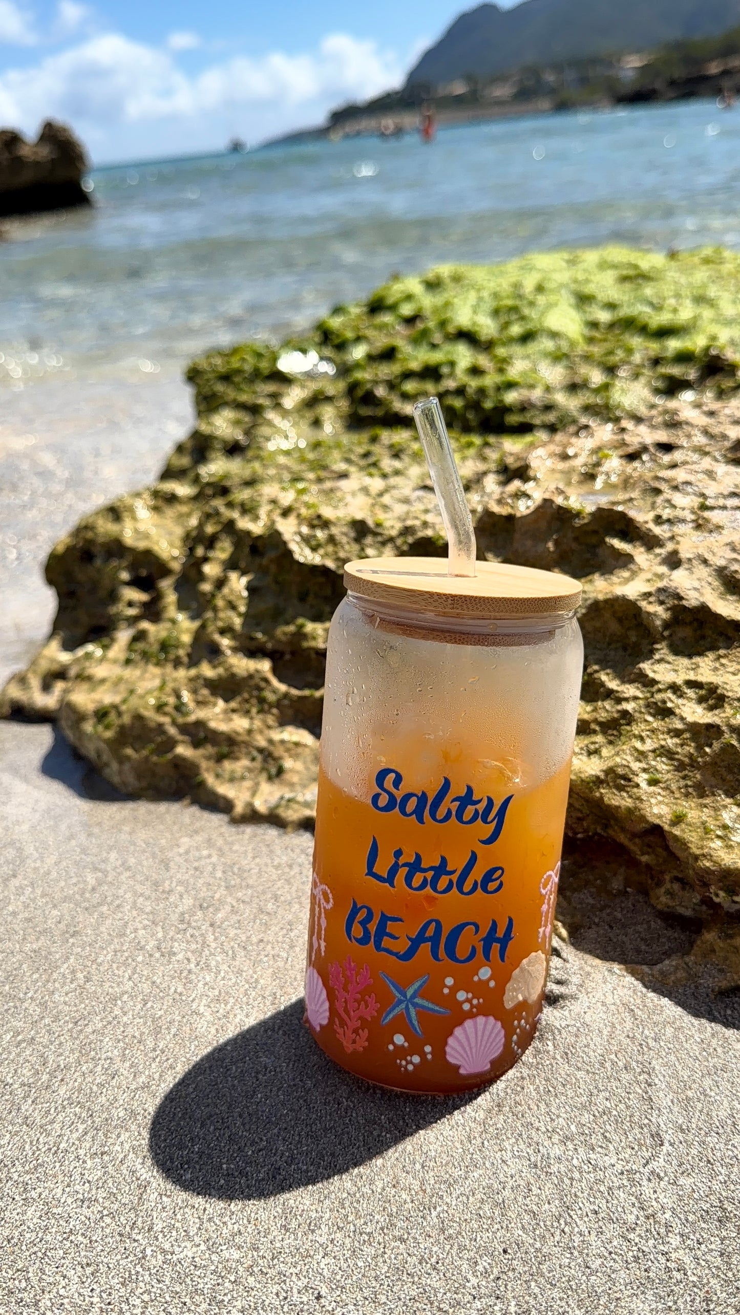 Tumbler with 'Salty Little Beach' text on a sandy beach with ocean in the background