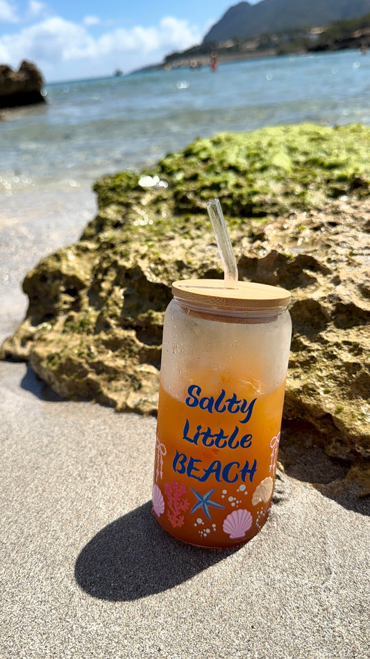 Tumbler with 'Salty Little Beach' text on a sandy beach with ocean in the background