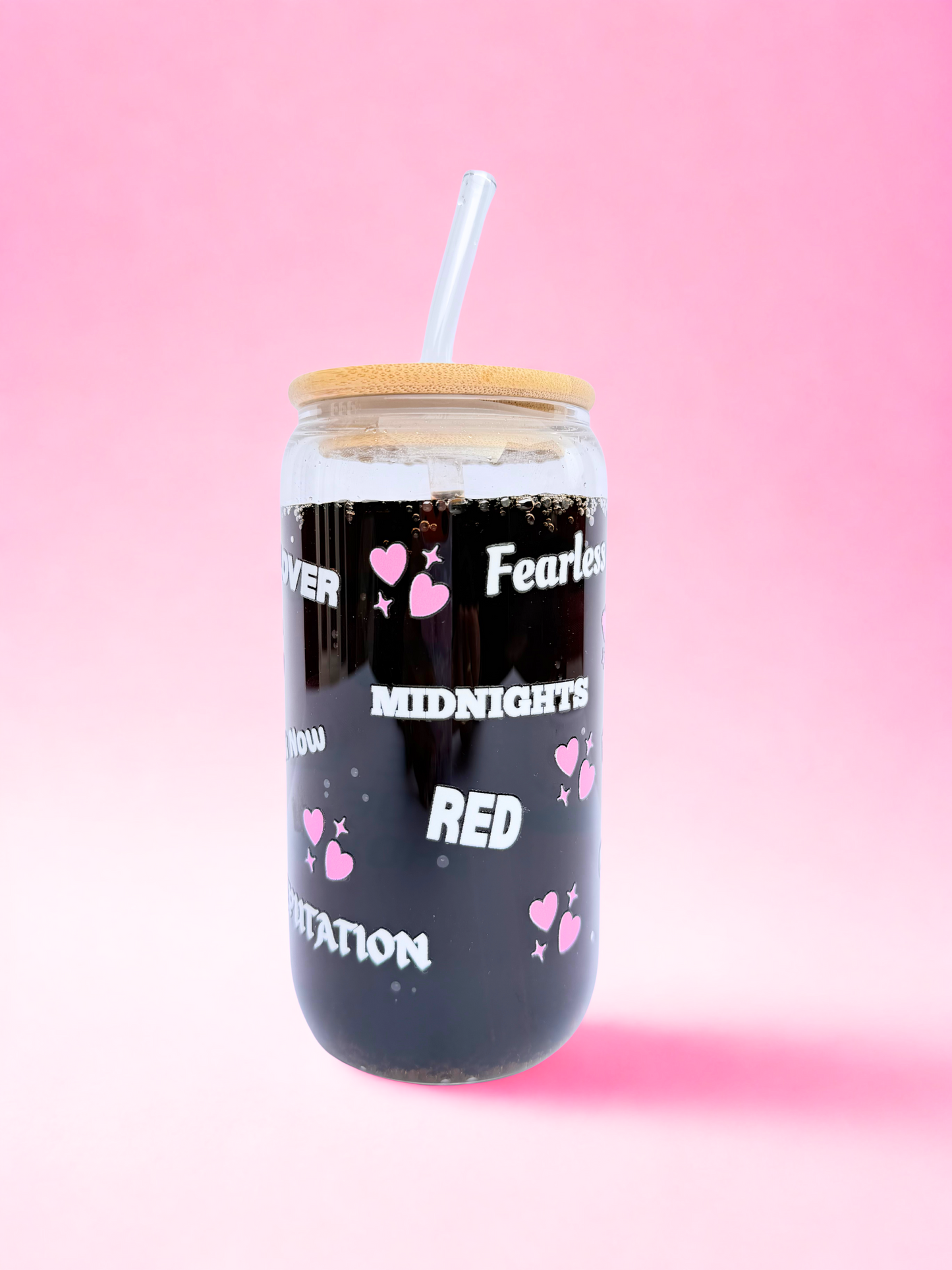 Glass tumbler with bamboo lid and straw, decorated with pink hearts and Taylor Swift Era names, including “The Life of a Showgirl,” on a pink background.