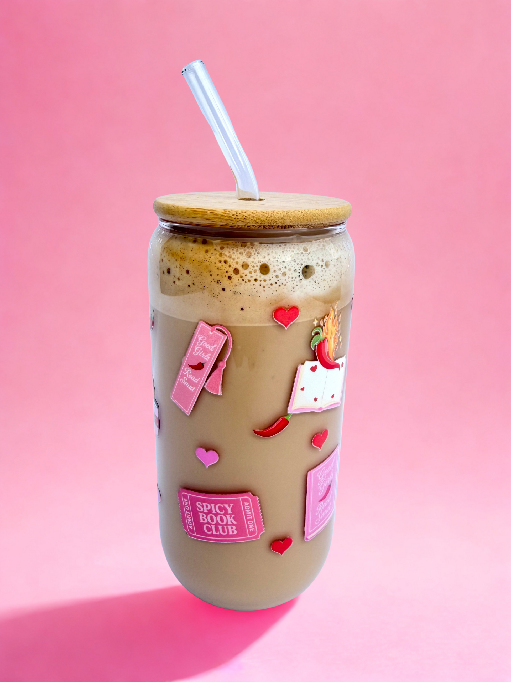 A 16oz glass with a bamboo lid and glass straw, featuring pink “Spicy Book Club” and “Good Girls Read Smut” designs with hearts and chilli peppers, on a pink background. Matching bookmark sold separately.