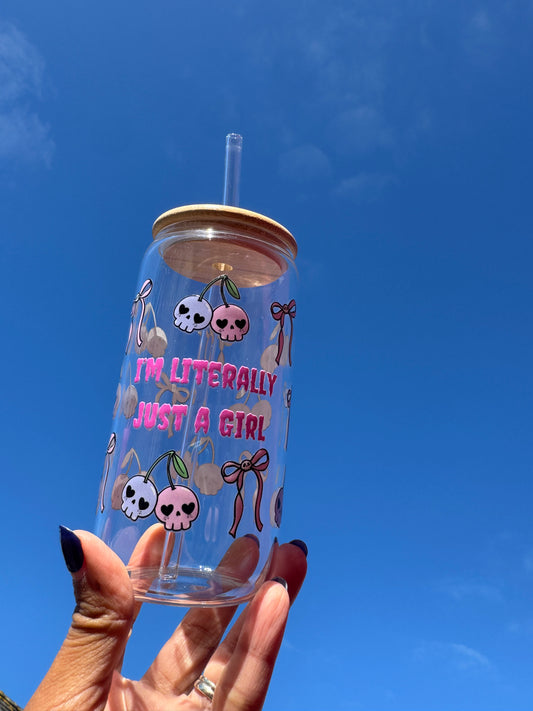 "A clear glass can cup with the phrase ‘I’m Literally Just a Girl’, decorated with pink and purple skulls styled as cherries with pink bows – a spooky cute Halloween design."