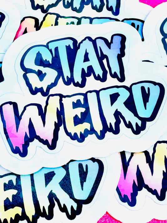 Vinyl sticker with the phrase ‘Stay Weird’ in bold rainbow-coloured font, photographed on a flat surface.