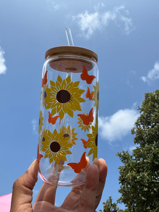 Clear glass can cup with bright sunflower and orange butterfly design, bamboo lid, and reusable glass straw, 16oz / 480ml capacity.