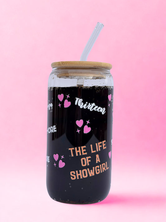 Glass tumbler with bamboo lid and straw, decorated with pink hearts and Taylor Swift Era names, including “The Life of a Showgirl,” on a pink background.