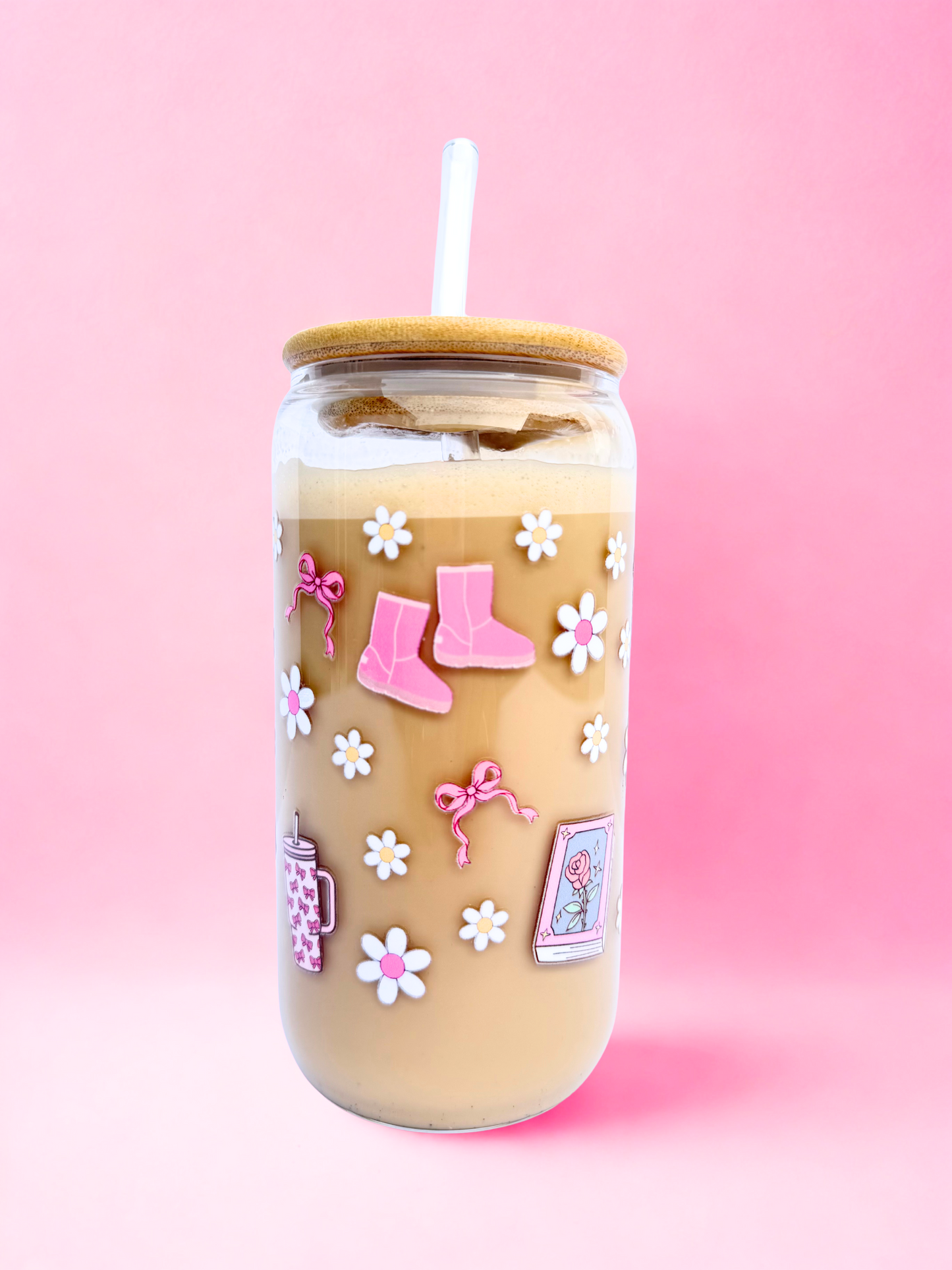A 16oz glass with a bamboo lid and glass straw, decorated with pink bows, daisies, boots, jumpers, and a candle that says “Smells like reading romance again” on a pink background. Matching bookmark sold separately.