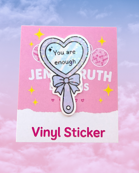 A heart-shaped mirror vinyl sticker with the text 'You are enough' is displayed on its pink backing card that reads 'JEMMARUTH Designs' and 'Vinyl Sticker' against a pastel pink and blue cloudy background.